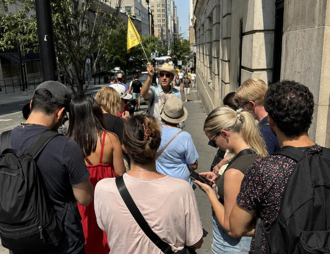 A group standing behind a tour guide holding a flag on a busy sidewalk